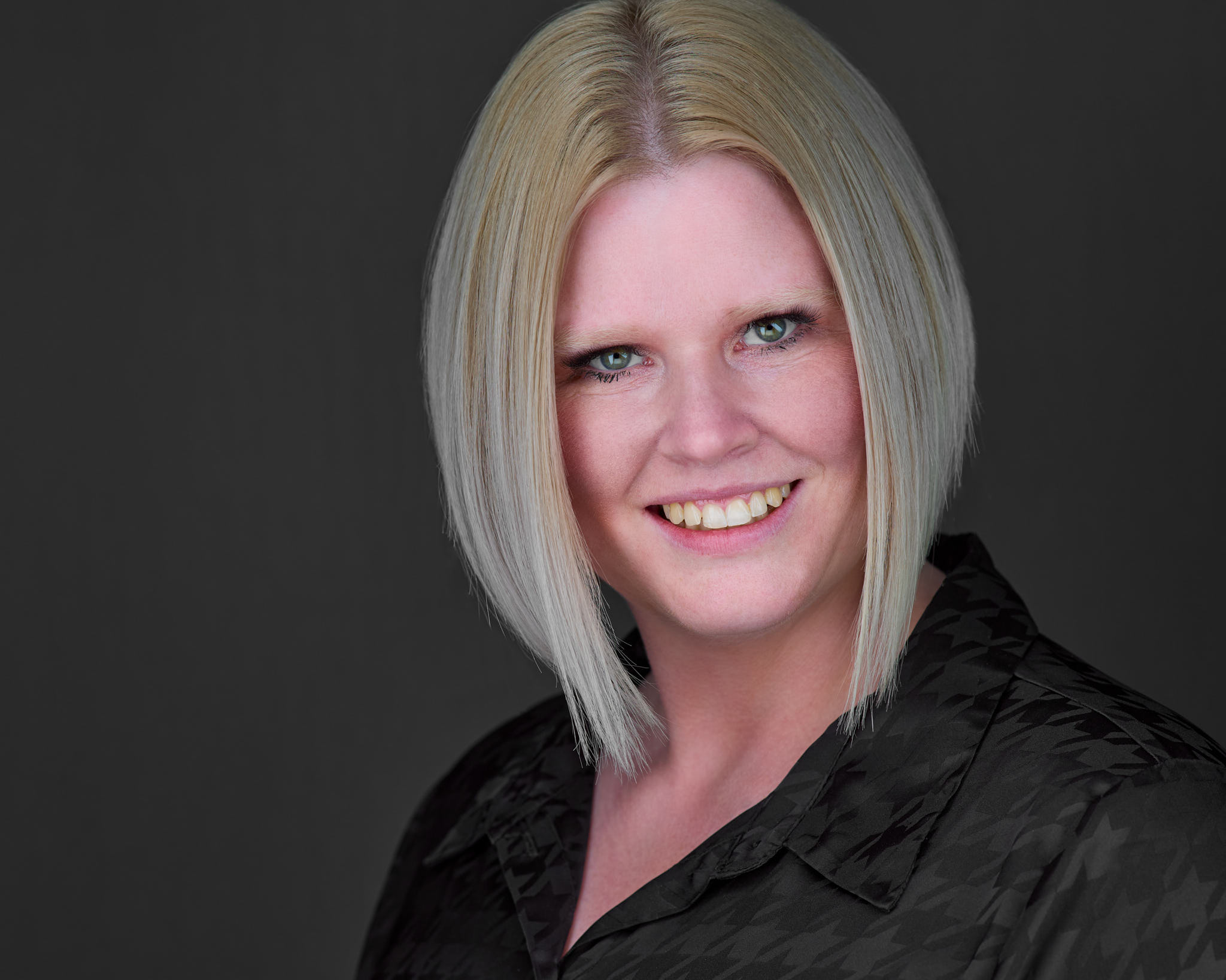 Business-Headshot einer blonden Frau im dunklen Oberteil vor anthrazitfarbenem Hintergrund, fotografiert von Christian Volk