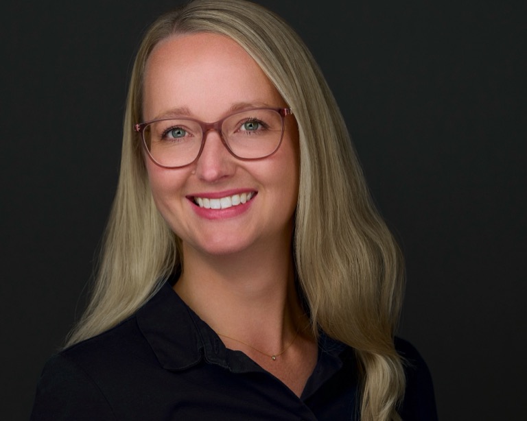 Business-Headshot einer jungen Frau mit Brille und Nadelstreifen-Blazer vor dunkelgrauem Hintergrund, fotografiert von Christian Volk