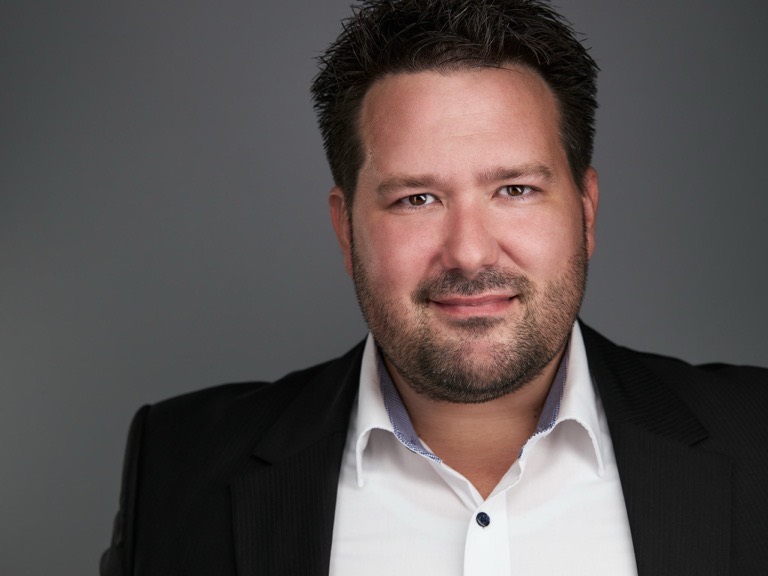 Business-Headshot eines Mannes mit Bart im schwarzen Anzug mit weißem Hemd vor grauem Hintergrund, fotografiert von Christian Volk