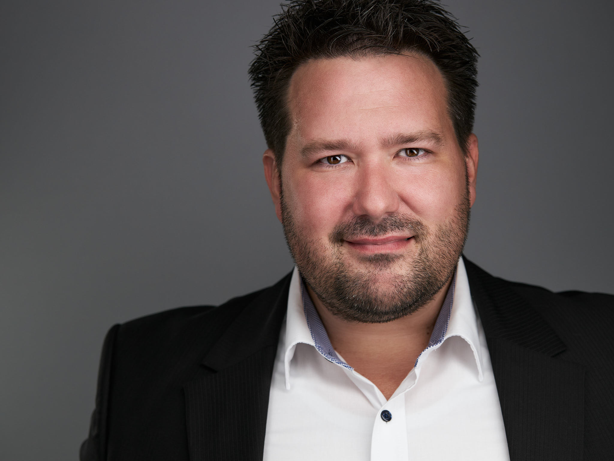 Business-Headshot eines Mannes mit Bart im schwarzen Anzug mit weißem Hemd vor grauem Hintergrund, fotografiert von Christian Volk