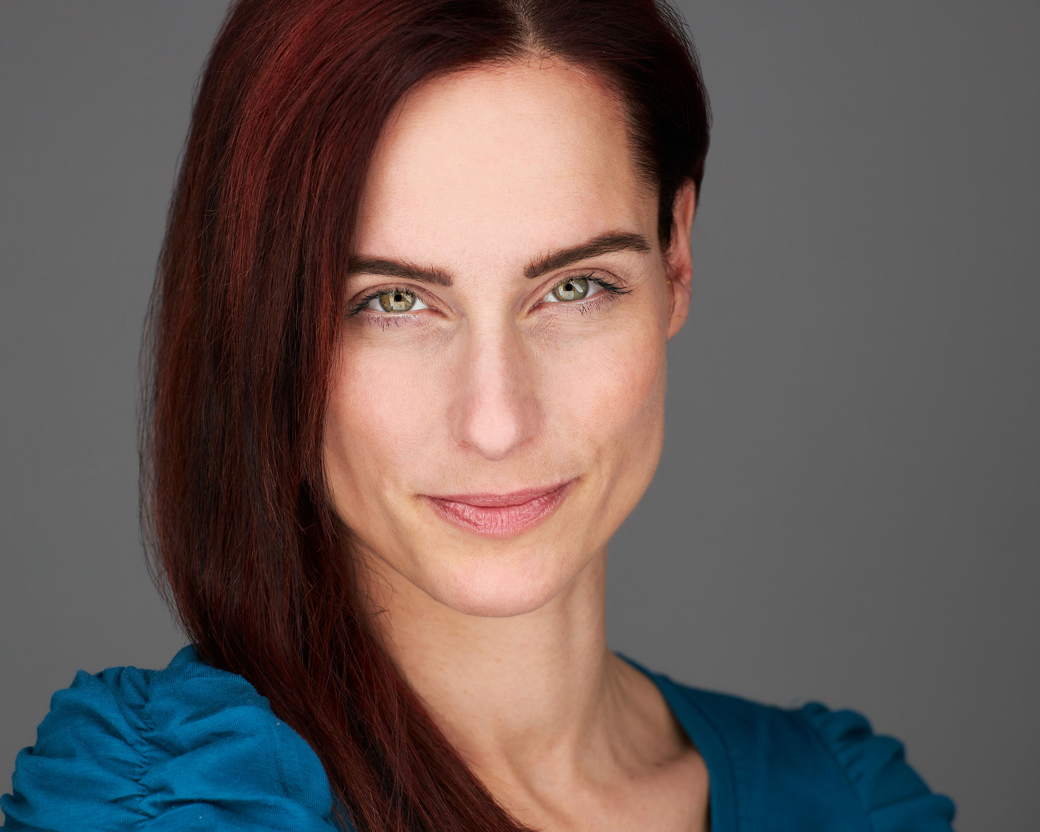 Schauspieler-Headshot einer Frau mit rotbraunem Haar vor grauem Hintergrund, fotografiert von Christian Volk