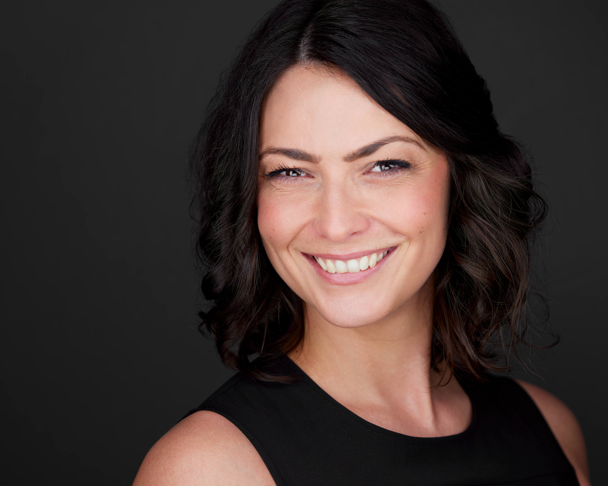 Schauspieler-Headshot einer Frau mit dunklen Locken vor dunklem Hintergrund, fotografiert von Christian Volk